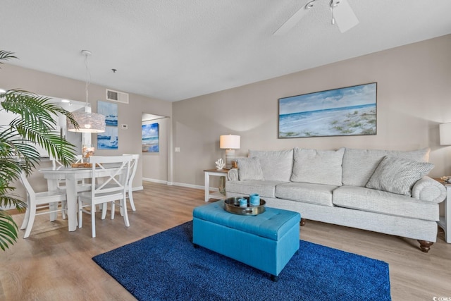 living area featuring ceiling fan, a textured ceiling, baseboards, and wood finished floors