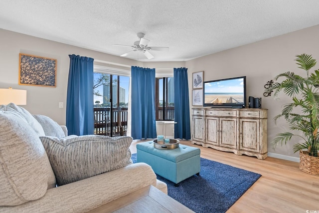 living area featuring light wood-type flooring, ceiling fan, baseboards, and a textured ceiling