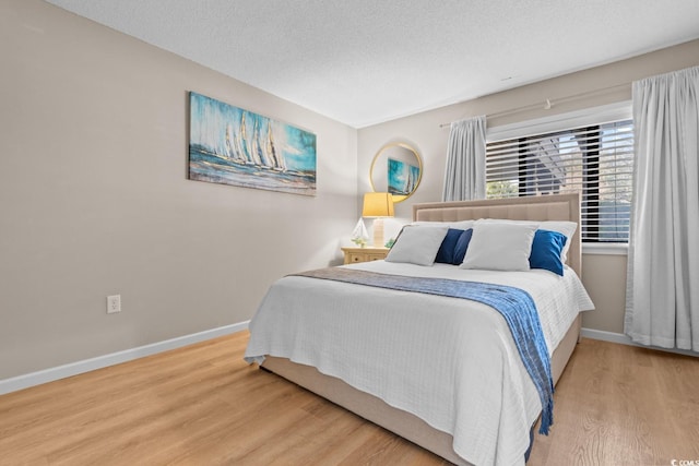 bedroom with a textured ceiling, baseboards, and wood finished floors