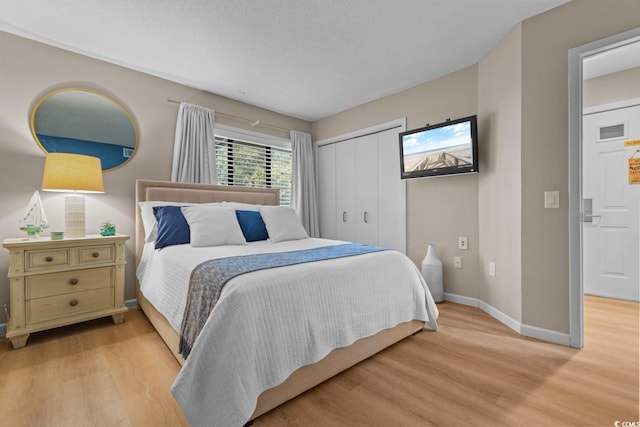 bedroom with a textured ceiling, light wood-style flooring, visible vents, baseboards, and a closet