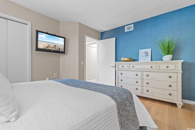 bedroom with baseboards, wood finished floors, visible vents, and wallpapered walls