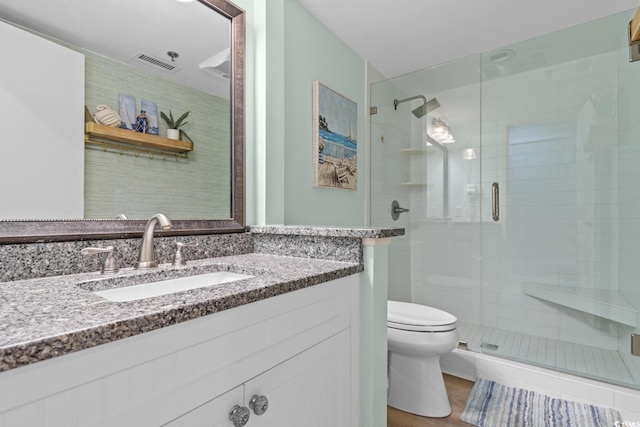 bathroom with toilet, vanity, a shower stall, and visible vents