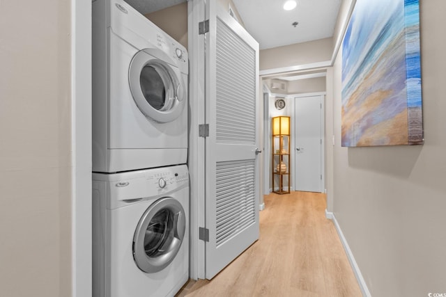 laundry area with light wood-type flooring, stacked washer and clothes dryer, baseboards, and laundry area