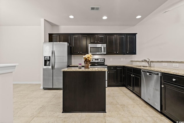 kitchen featuring light stone counters, stainless steel appliances, visible vents, a sink, and a kitchen island