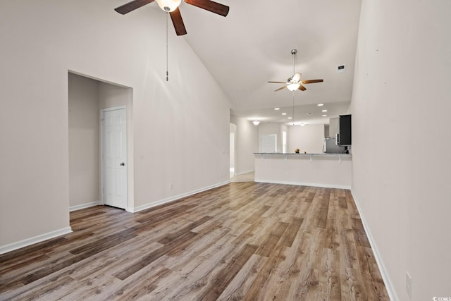 unfurnished living room with baseboards, ceiling fan, high vaulted ceiling, and wood finished floors