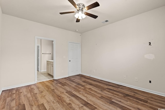 unfurnished bedroom with visible vents, ensuite bath, baseboards, and wood finished floors