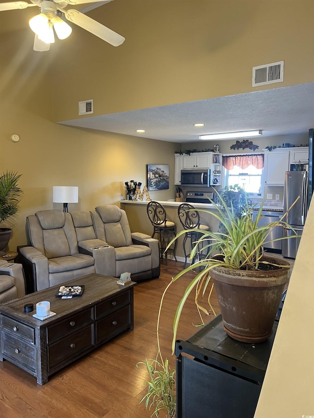 living room with wood finished floors, visible vents, and a ceiling fan