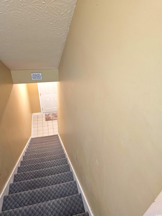 stairway featuring carpet floors, baseboards, visible vents, and a textured ceiling