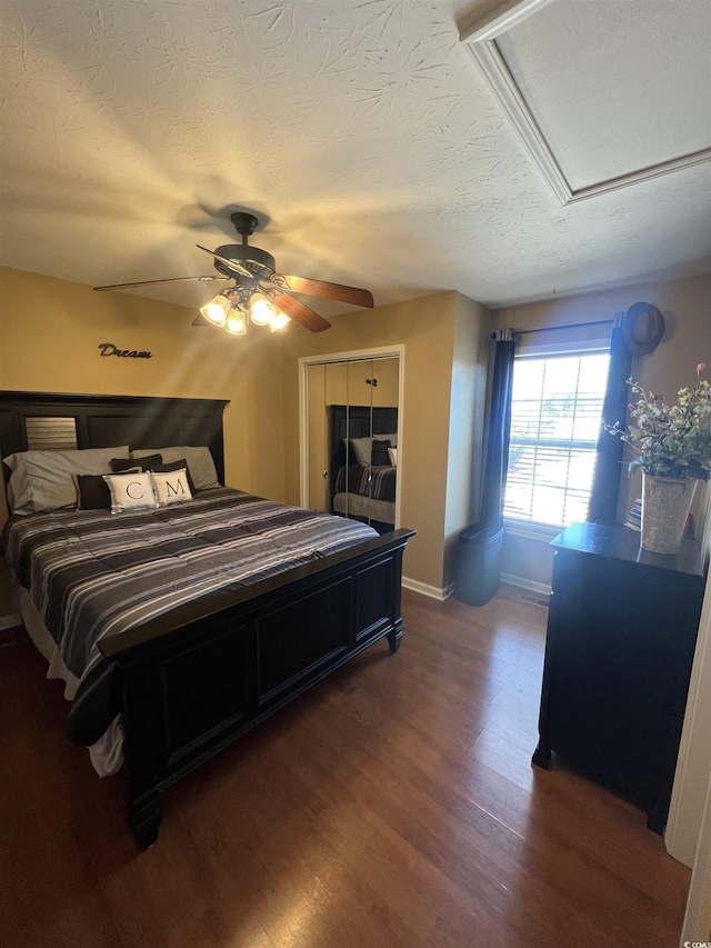 bedroom with a textured ceiling, wood finished floors, a ceiling fan, baseboards, and attic access