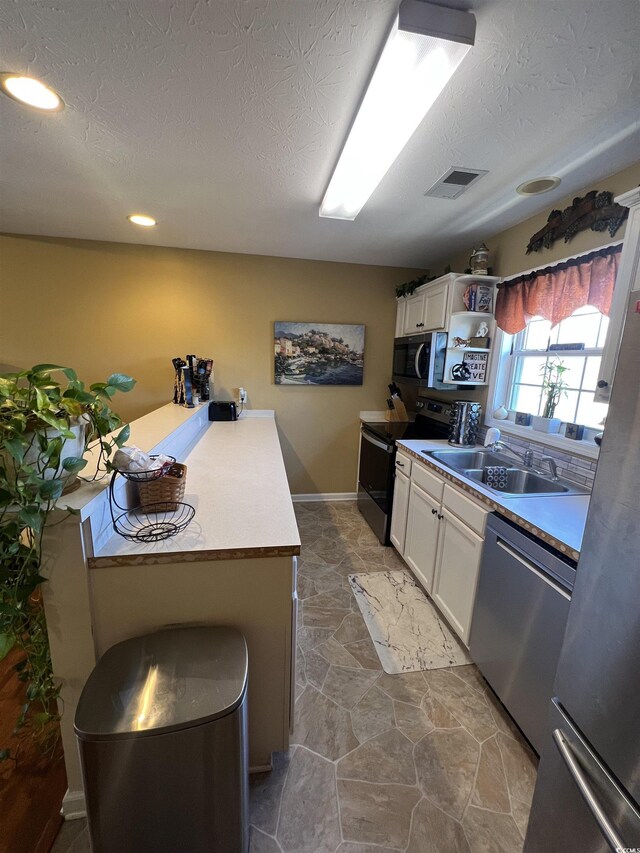 kitchen featuring white cabinets, a textured ceiling, stainless steel appliances, and a sink