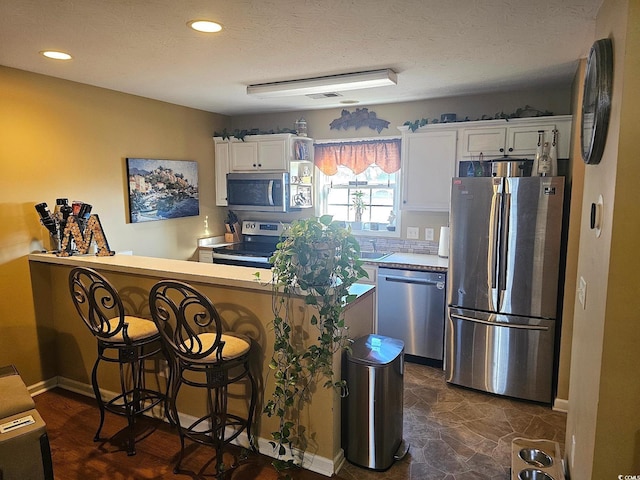 kitchen featuring a textured ceiling, a breakfast bar area, a peninsula, white cabinets, and appliances with stainless steel finishes