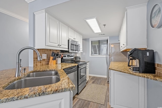 kitchen with a sink, white cabinetry, appliances with stainless steel finishes, backsplash, and light wood finished floors