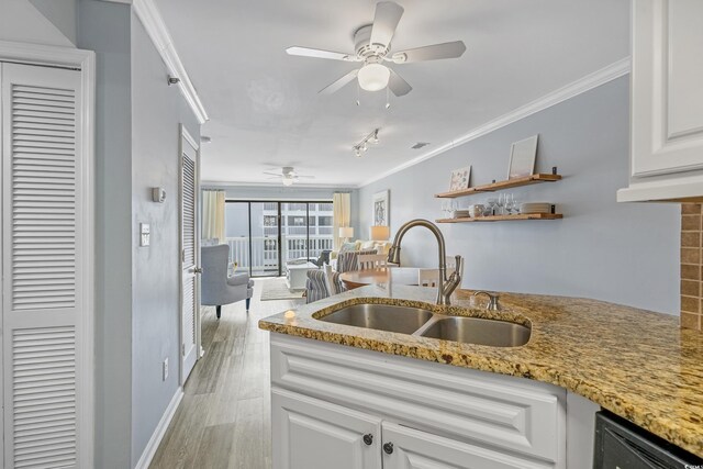 kitchen with light stone counters, a sink, white cabinetry, light wood-style floors, and crown molding