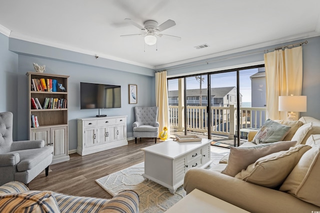 living room featuring a ceiling fan, visible vents, wood finished floors, and ornamental molding