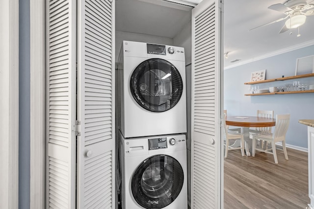 clothes washing area featuring stacked washer / drying machine, ornamental molding, a ceiling fan, wood finished floors, and laundry area