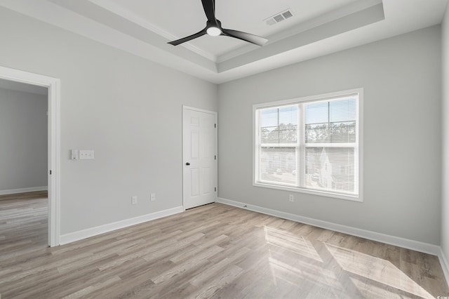 empty room with ceiling fan, visible vents, light wood-style floors, baseboards, and a raised ceiling