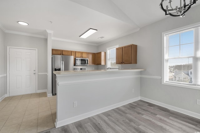 kitchen featuring stainless steel appliances, light countertops, brown cabinetry, and a peninsula