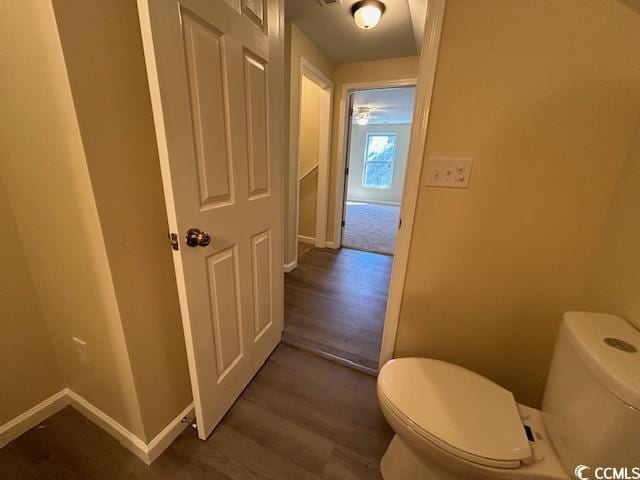 half bath featuring baseboards, toilet, and wood finished floors