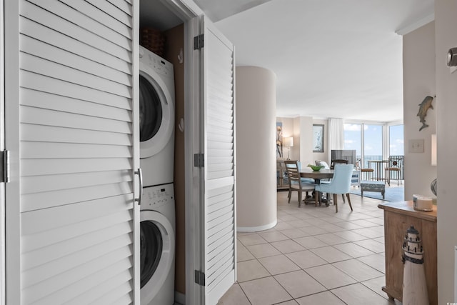 clothes washing area with stacked washing maching and dryer, light tile patterned floors, and laundry area