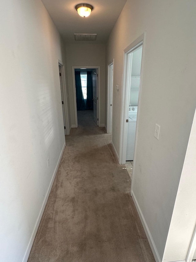 corridor with washer / clothes dryer, light colored carpet, visible vents, and baseboards