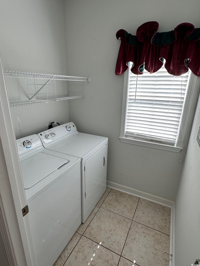 clothes washing area with laundry area, washing machine and dryer, light tile patterned floors, and baseboards