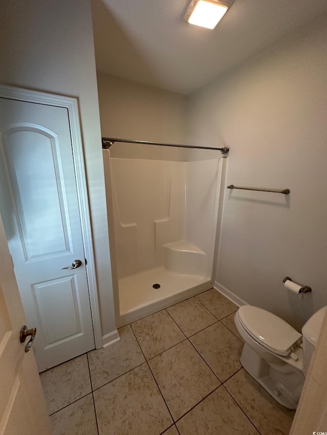 bathroom featuring a shower, tile patterned flooring, baseboards, and toilet