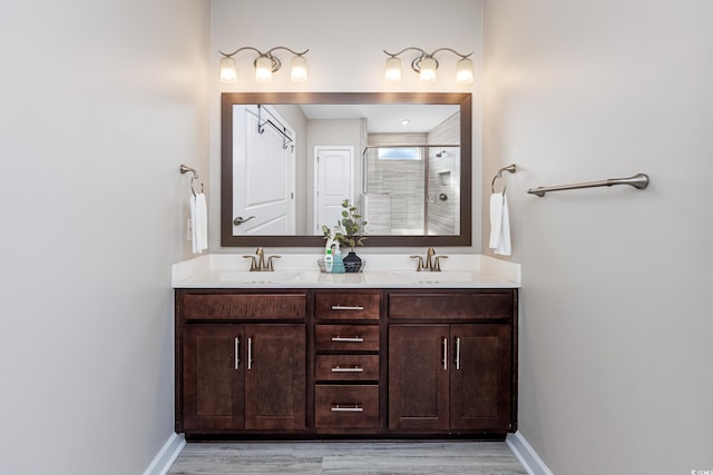 bathroom with double vanity, a stall shower, baseboards, and a sink