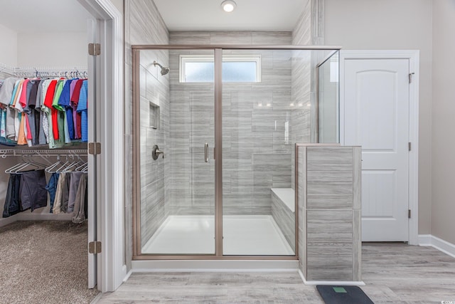 full bathroom featuring a spacious closet, a stall shower, wood finished floors, and baseboards