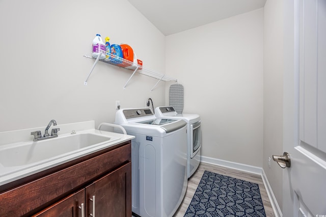 clothes washing area with cabinet space, light wood-style flooring, a sink, independent washer and dryer, and baseboards