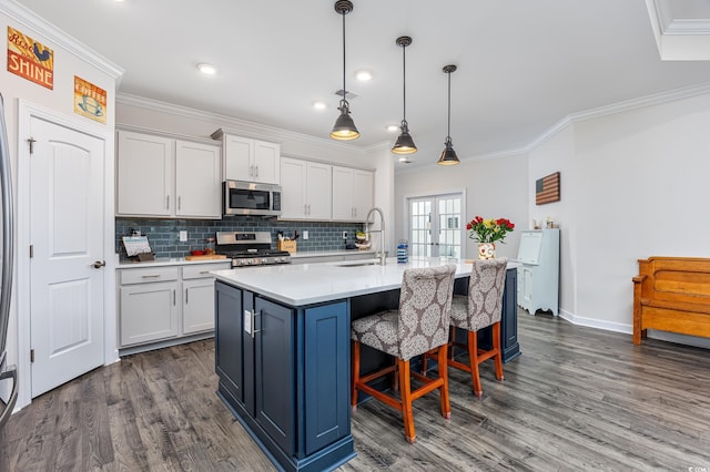 kitchen with stainless steel appliances, light countertops, dark wood-type flooring, ornamental molding, and a sink