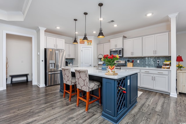 kitchen featuring visible vents, light countertops, ornamental molding, appliances with stainless steel finishes, and a center island with sink