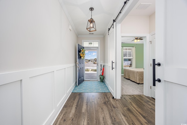 doorway to outside featuring a barn door, a wainscoted wall, ornamental molding, dark wood-style flooring, and a decorative wall