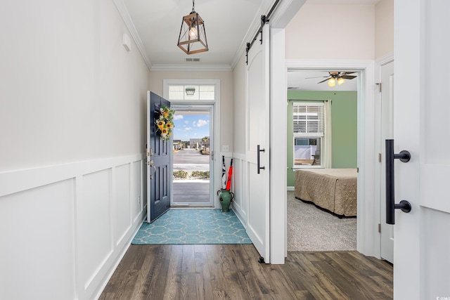 doorway to outside featuring dark wood-style flooring, crown molding, visible vents, a decorative wall, and a barn door