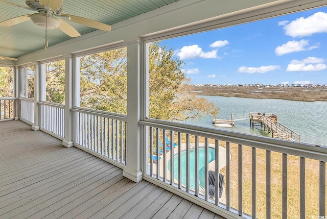 wooden terrace featuring a water view, ceiling fan, an outdoor pool, and a boat dock