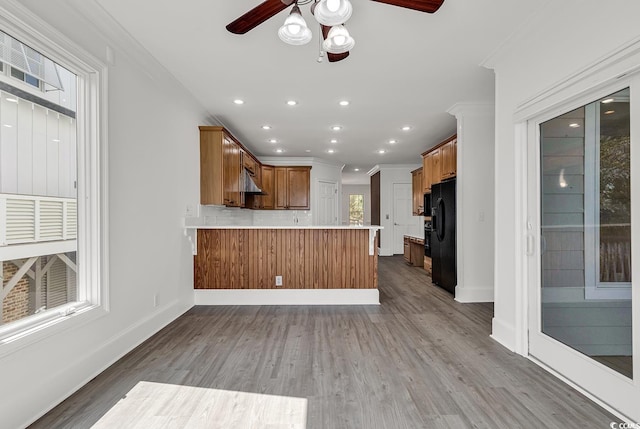 kitchen with black fridge with ice dispenser, wood finished floors, a peninsula, light countertops, and crown molding