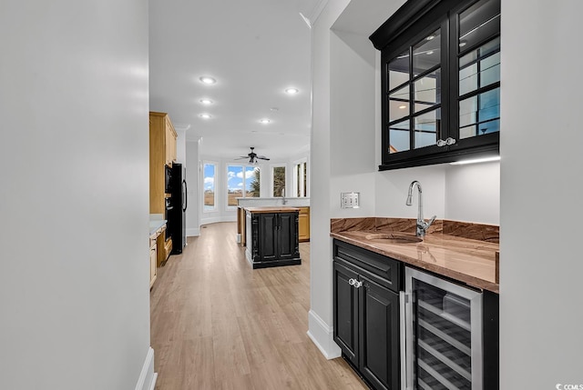 bar with light wood finished floors, wine cooler, freestanding refrigerator, wet bar, and a sink