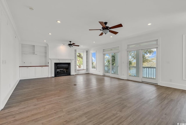 unfurnished living room featuring crown molding, recessed lighting, a fireplace, and wood finished floors