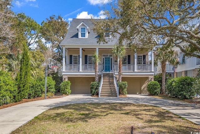 raised beach house featuring concrete driveway, an attached garage, covered porch, stairs, and a front lawn