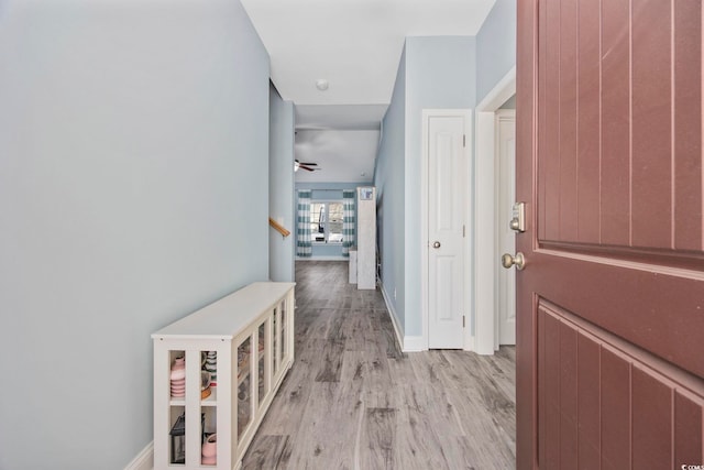 hall with baseboards, stairway, and light wood finished floors