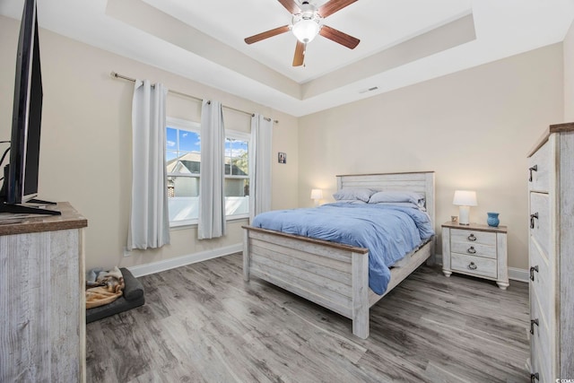 bedroom featuring ceiling fan, wood finished floors, visible vents, baseboards, and a tray ceiling