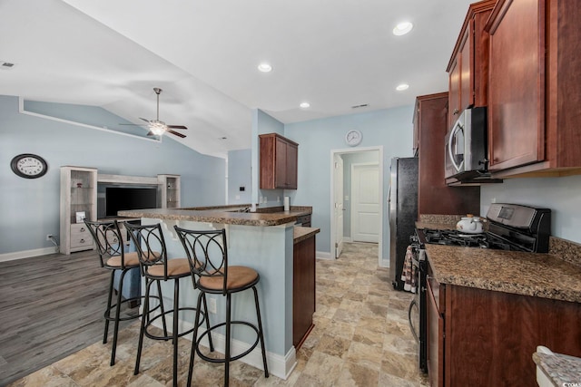 kitchen featuring stainless steel appliances, lofted ceiling, a kitchen bar, a ceiling fan, and baseboards