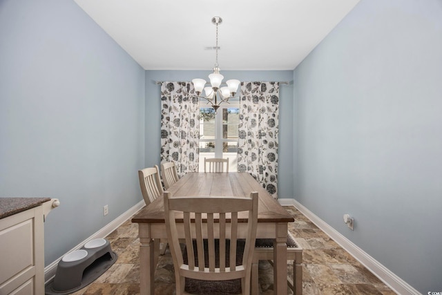 dining space featuring a chandelier, stone finish floor, and baseboards