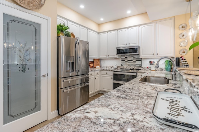 kitchen featuring light stone countertops, a sink, white cabinets, appliances with stainless steel finishes, and decorative backsplash