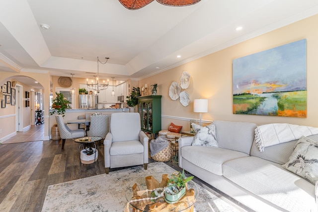 living room featuring arched walkways, a raised ceiling, an inviting chandelier, ornamental molding, and wood finished floors