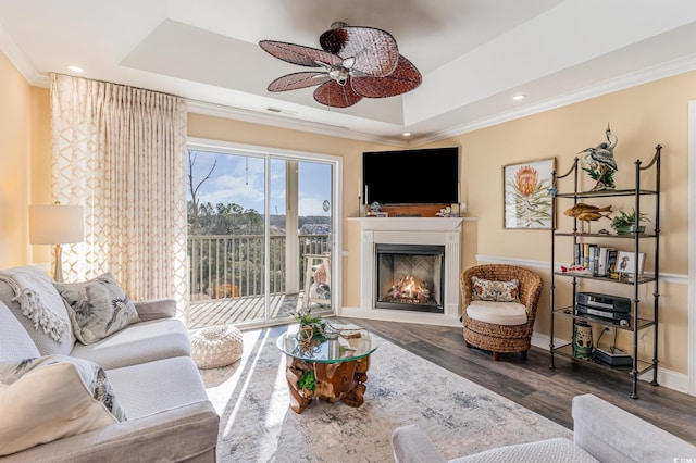 living area with wood finished floors, a raised ceiling, and crown molding