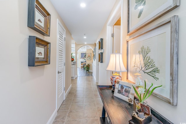 hall featuring light tile patterned floors, baseboards, arched walkways, and recessed lighting