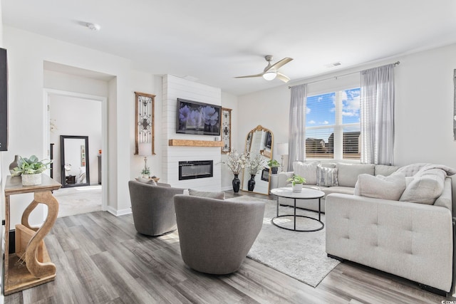 living room featuring a large fireplace, wood finished floors, visible vents, a ceiling fan, and baseboards