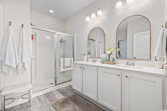 full bath featuring double vanity, wood finished floors, a stall shower, and a sink