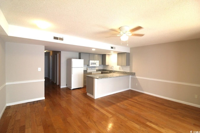 kitchen featuring white appliances, dark wood-style floors, a peninsula, gray cabinetry, and a sink