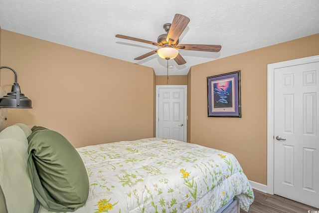 bedroom with a textured ceiling, ceiling fan, wood finished floors, and baseboards